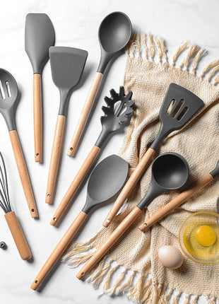Set of kitchen utensils with wooden handles on a light surface.