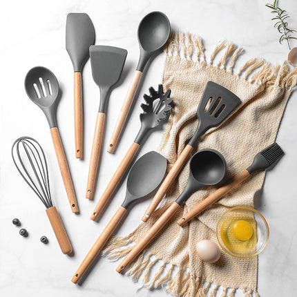 Set of kitchen utensils with wooden handles on a light surface.