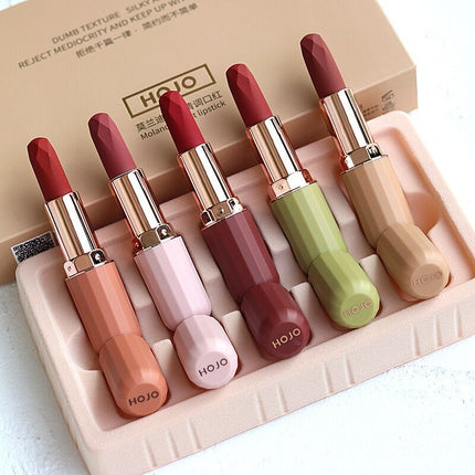 A set of five HOJO lipsticks in various colors displayed in a box with a velvet texture finish.