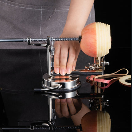 Person using an apple peeler with a sliced apple on a reflective surface.