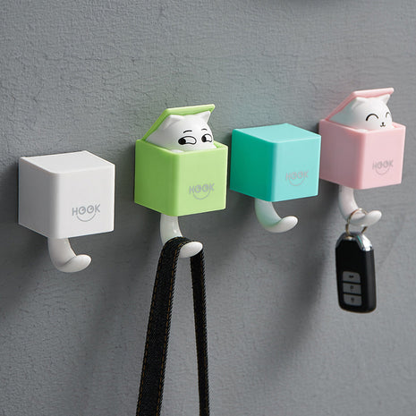 Four colorful wall hooks with cartoon designs on a gray wall.