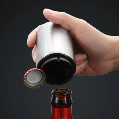 Hand using a bottle opener to remove a cap from a beer bottle on a black background