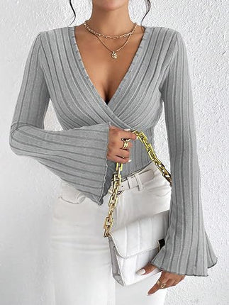 Person wearing a gray ribbed long-sleeve top with a deep neckline, holding a gold chain bag against a white background.