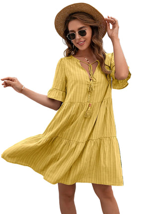 Woman wearing a yellow dress and straw hat in front of a white wall with greenery.