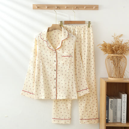 Floral pajama set hanging on a wooden hanger against a white wall with a vase of dried plants and books on a shelf.