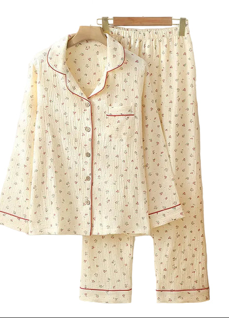 Floral pajama set hanging on a wooden hanger against a white wall with a vase of dried plants and books on a shelf.