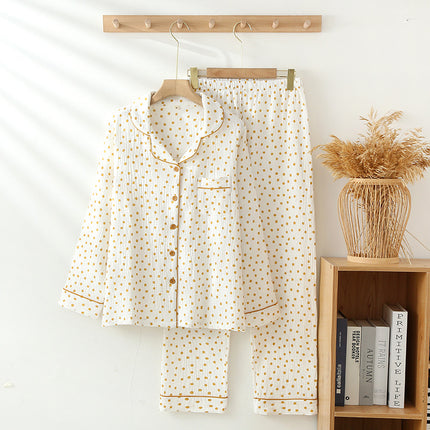 White pajama set with gold polka dots on a hanger against a white wall with a wooden shelf in the background.
