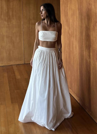 Woman wearing a white outfit standing against a wooden wall.