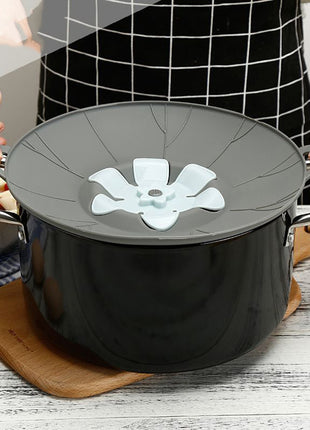 Black pot with a gray lid featuring a white floral design on a wooden surface.