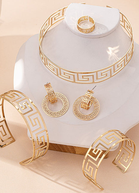 Gold jewelry set including bracelet, ring, and earrings on a white stand with a beige background
