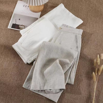 Light gray linen pants on a brown fabric surface with a magazine and small wooden item.
