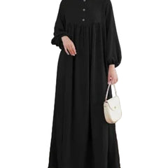 Person wearing a black dress holding a white handbag in a minimalistic room.