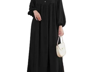 Person wearing a black dress holding a white handbag in a minimalistic room.