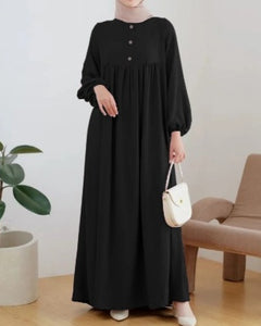 Person wearing a black dress holding a white handbag in a minimalistic room.