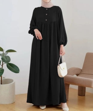Person wearing a black dress holding a white handbag in a minimalistic room.