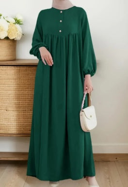 Person wearing a long green dress holding a white handbag indoors.