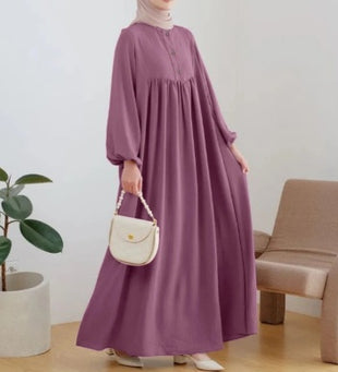 Person wearing a long purple dress holding a white handbag indoors.