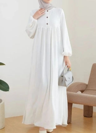 Person wearing a white dress holding a gray handbag in a minimalistic room.