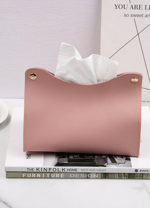 Pink tissue holder with tissues on top of a book with a cup and saucer in the background.