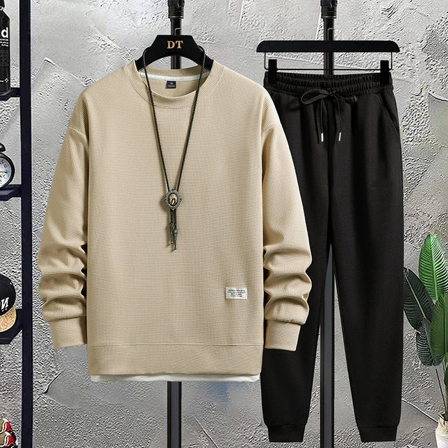 Beige sweatshirt and black pants on hangers against a textured wall.