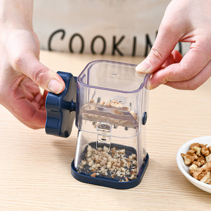 Hand using a small food grinder with walnuts on a wooden surface.