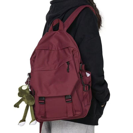 Person wearing a maroon backpack with a small green frog plush toy attached, on a white background