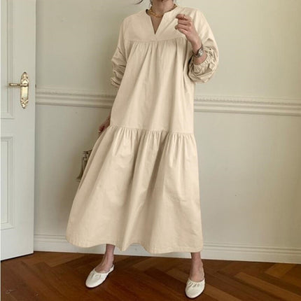 Person wearing a beige dress in an indoor setting with wooden flooring and white walls.