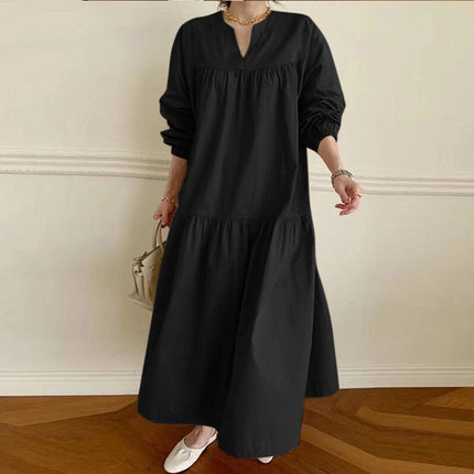 Person wearing a black long-sleeve dress against a white wall.