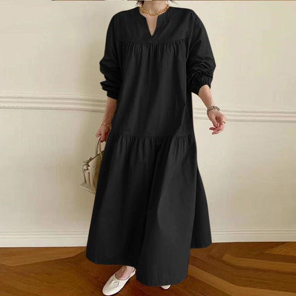 Person wearing a black long-sleeve dress against a white wall.