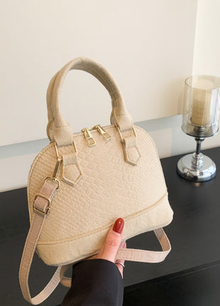 Beige handbag held by a hand with red nail polish on a dark surface.
