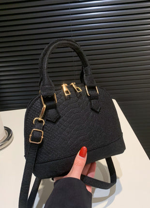 Black textured handbag with gold accents held by a hand against a neutral background