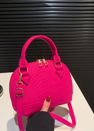 Pink handbag with gold accents held by a hand on a white surface with a black background