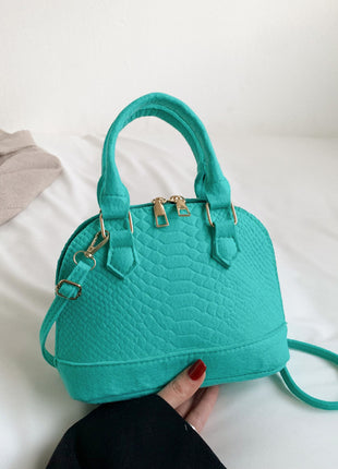 Turquoise handbag held by a person on a white surface