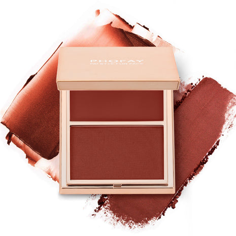 A selection of PHOFAY Duo Cream & Powder Blush products displayed on a pink surface, with the words 'JUST ENOUGH' visible in the image. The products come in golden-colored compact cases with brushes on one side and pink and red blush shades on the other.