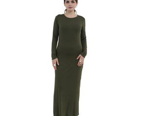 Woman wearing a long green dress standing in a minimalistic room with a white chair and decorative plant.