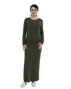 Woman wearing a long green dress standing in a minimalistic room with a white chair and decorative plant.