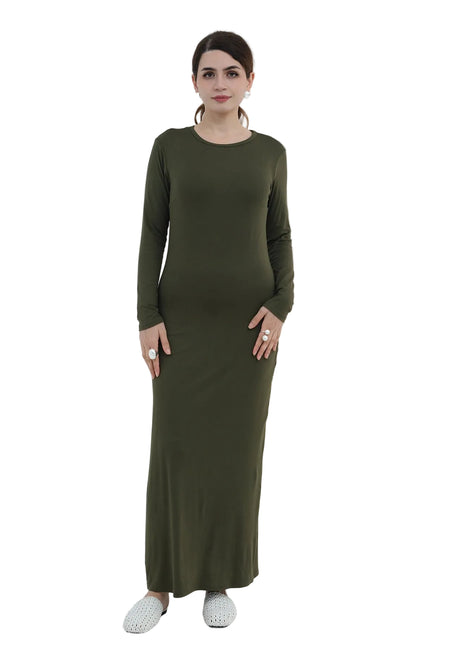 Woman wearing a long green dress standing in a minimalistic room with a white chair and decorative plant.