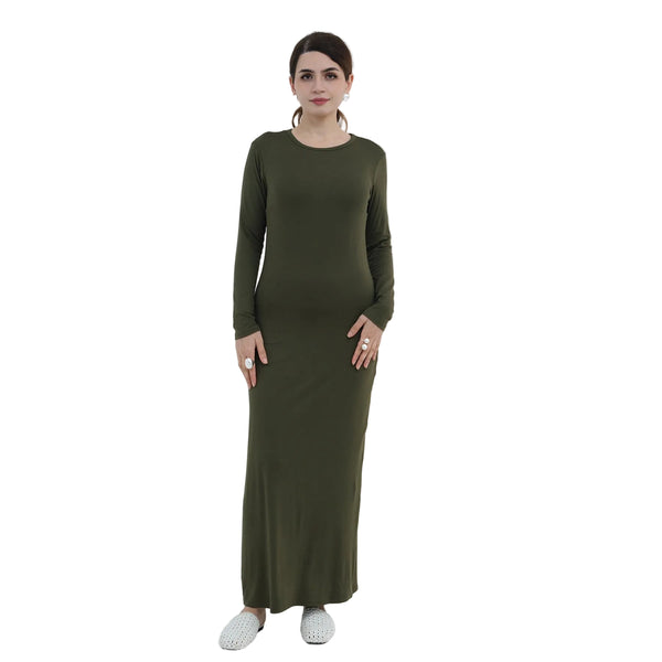 Woman wearing a long green dress standing in a minimalistic room with a white chair and decorative plant.
