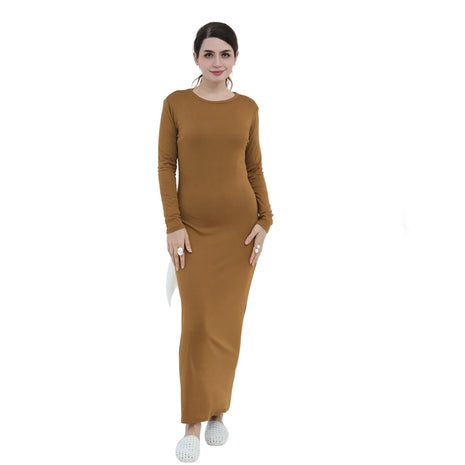 Woman wearing a brown dress standing in a minimalistic room with a vase and chair.
