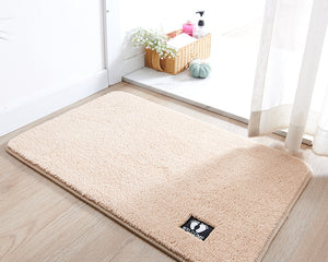 Beige rug with a brand logo on a wooden floor in a room with a window and basket.