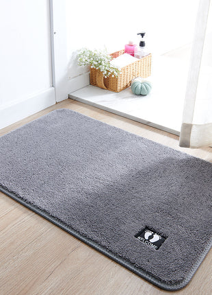 Gray doormat with a brand logo on a wooden floor in a bright room.