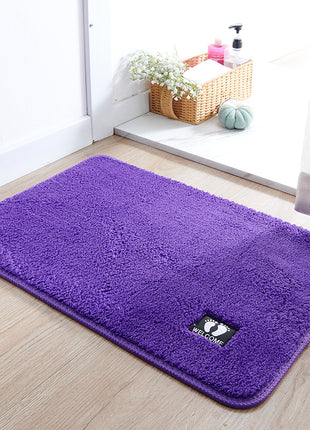 Purple welcome mat on a wooden floor with a basket of flowers in the background.