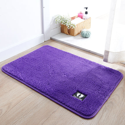 Purple welcome mat on a wooden floor with a basket of flowers in the background.