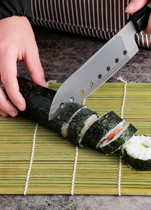 Person cutting sushi with a knife on a bamboo mat
