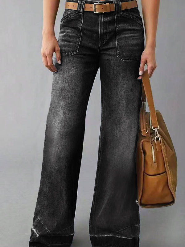 Person wearing black wide-leg jeans holding a brown leather bag on a gray background blndl