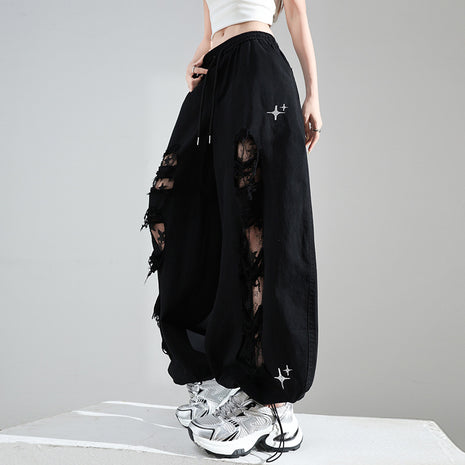 Person wearing black distressed pants with white sneakers on a gray background