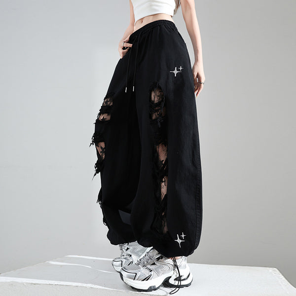 Person wearing black distressed pants with white sneakers on a gray background