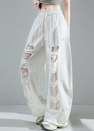 White pants with sheer panels worn by a person on a gray background