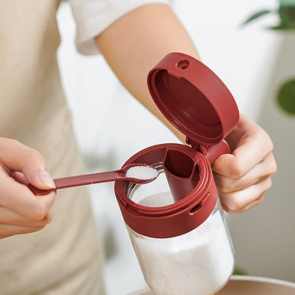 Person using a red measuring spoon to add salt to a clear container.