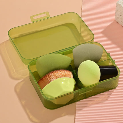 Set of makeup sponges and brushes in a green case on a pink surface